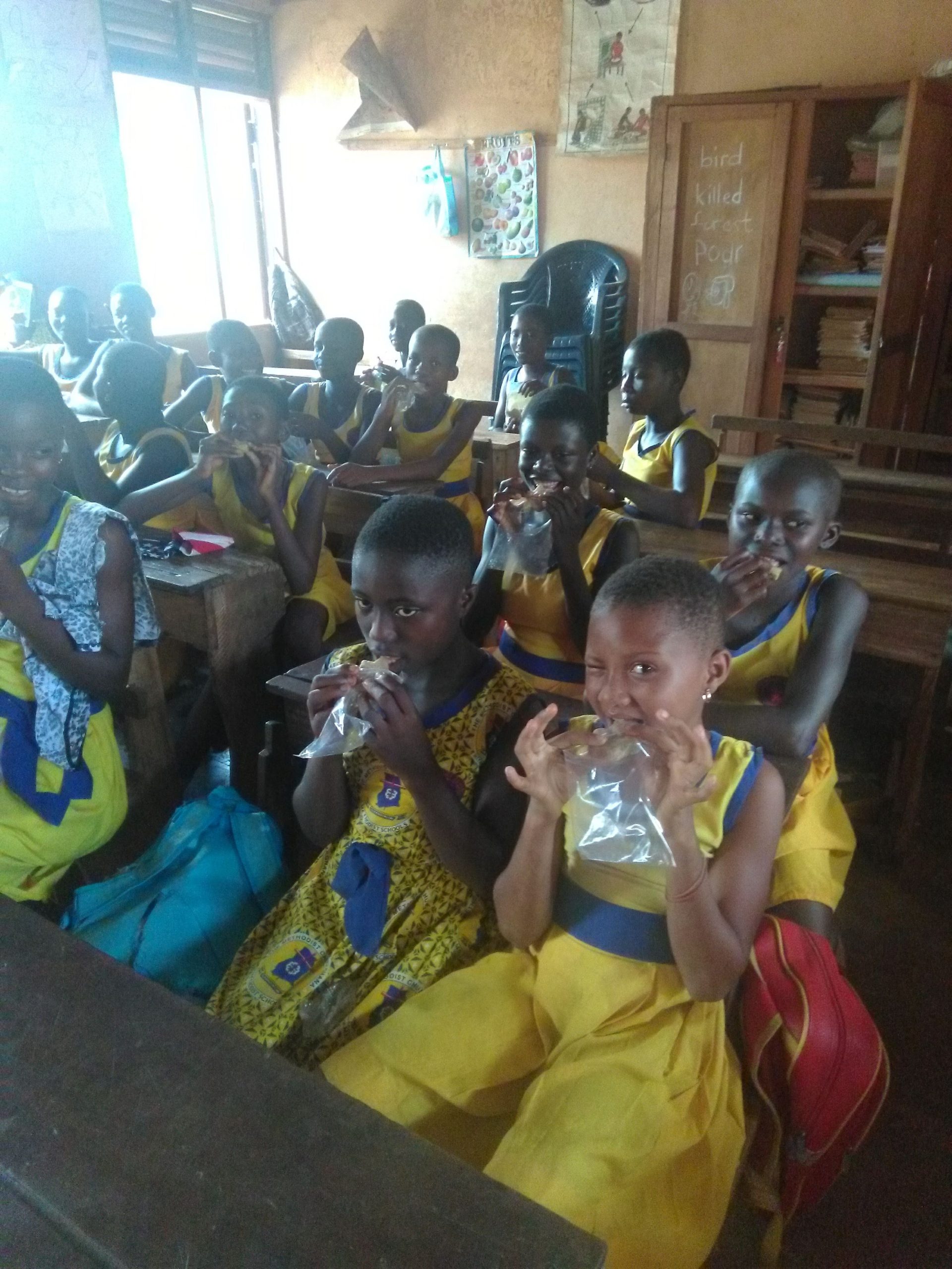 A classroom full of young students dressed in yellow and blue uniforms, sitting at wooden desks.