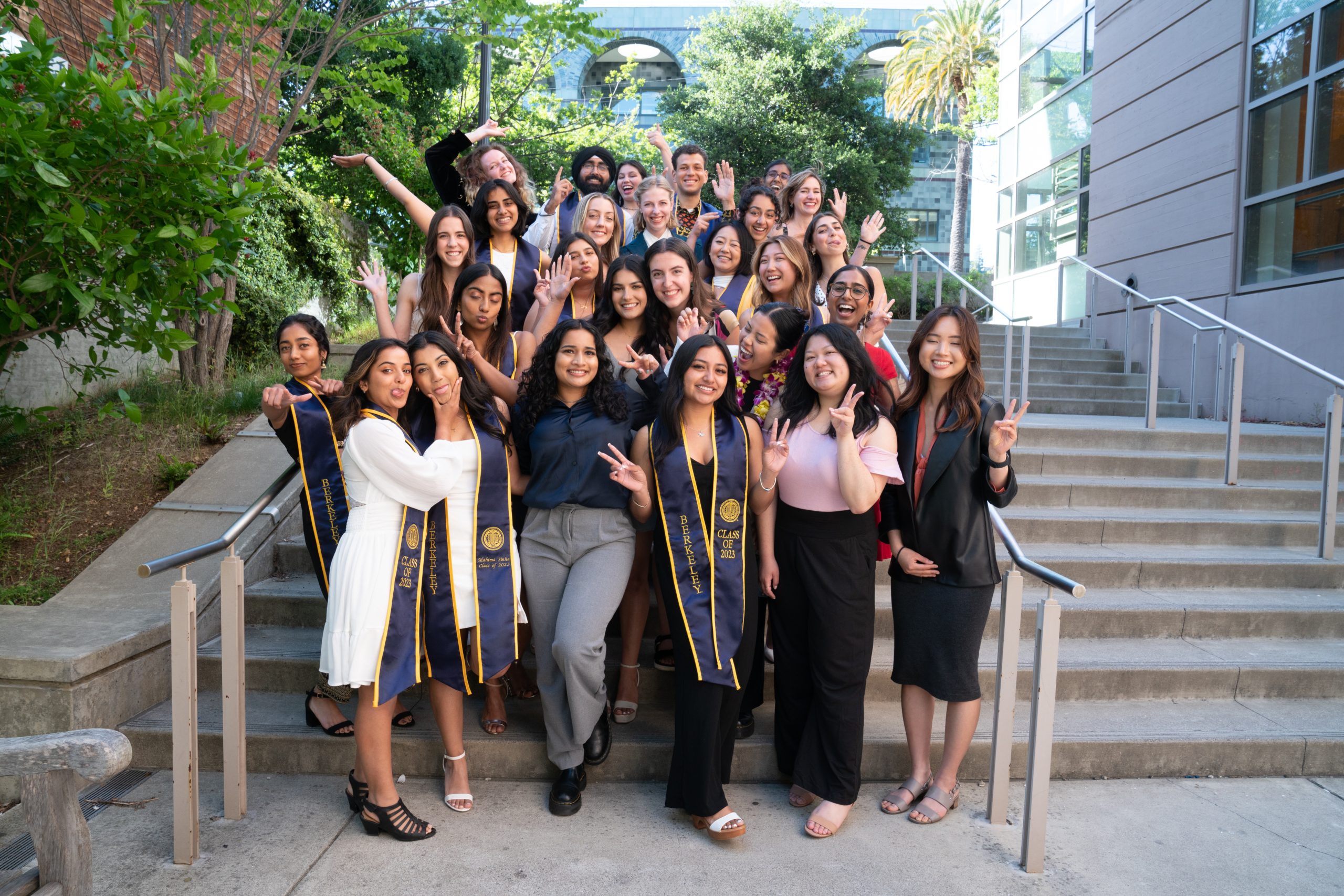 The Global Poverty and Practice minor Class of 2023 posing for graduation photo while wearing sashes and smiling happily.